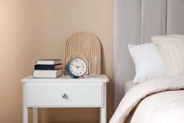 Yatağın yanında kitap, dekor ve alarmlı bir masa var.