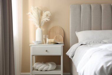 Yatağın yanında kitap, dekor ve bir bardak su olan komodin.