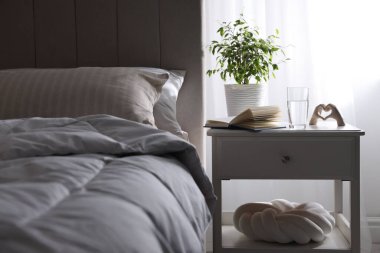 Yatağın yanında kitap, dekor ve bir bardak su olan komodin.