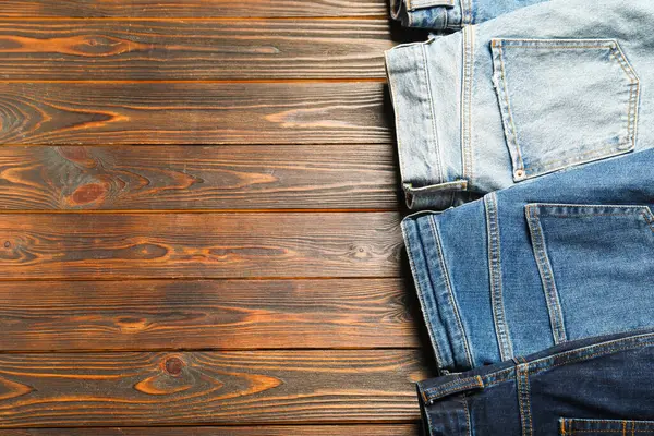 Different stylish jeans on wooden background, flat lay. Space for text