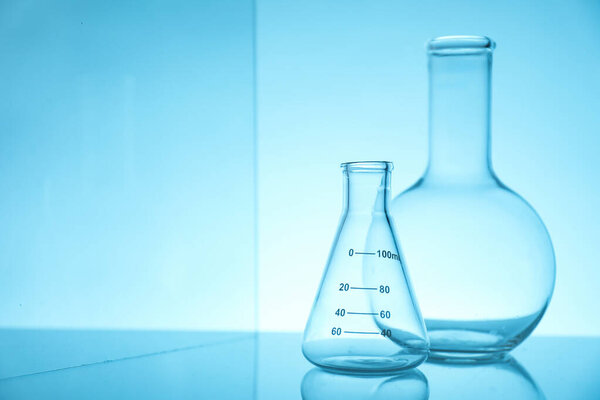 Empty flasks on mirror surface against light blue background, space for text. Laboratory equipment
