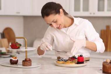 Şekerci masadaki tartın üzerine pudra şekeri serpiyor.