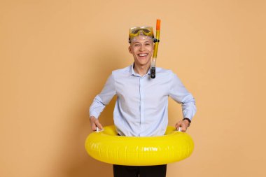 Şişme yüzüklü ve bej arka planda şnorkelle yüzen bir iş adamı.