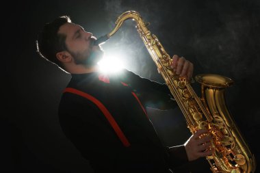 Profesyonel müzisyen siyah arkaplanda dumanla saksafon çalıyor.