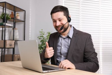 Gülümseyen çevrimiçi hoparlör. İçerideki masada dizüstü bilgisayarı var.