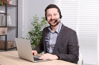 Gülümseyen çevrimiçi hoparlör. İçerideki masada dizüstü bilgisayarı var.