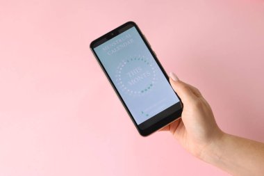 Regl. Pembe arka planda periyot takvim uygulaması olan akıllı telefonu tutan kadın, yukarıda görünüm