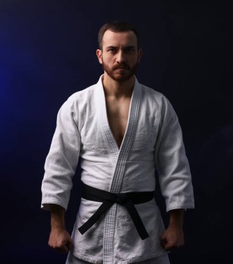 Üniformalı bir adam karanlık arka planda karate yapıyor.