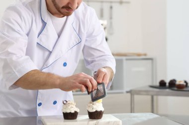 Şekerci çikolatayı mutfaktaki masada kekin üzerine rendeliyor, mesaj için yer var.