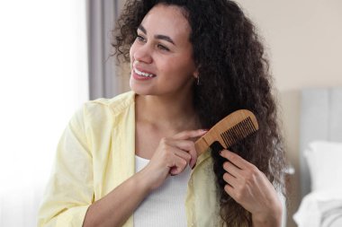 Gülümseyen genç kadın evde tarağıyla kıvırcık saçlarını tarıyor.