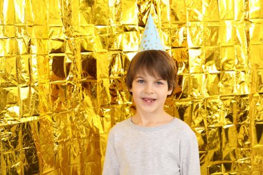 Altın folyo perdenin yanında, kağıt şapkalı şirin bir çocuk. Doğum günü sürpriz partisi