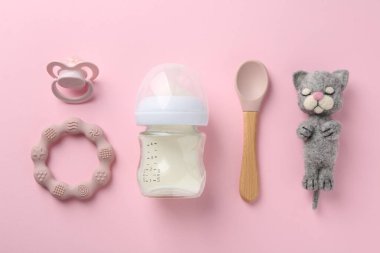 Sütlü beslenme şişesi, keçeli kedi, kaşık, emzik ve pembeleştirici pembe arka planda düz yatıyordu.