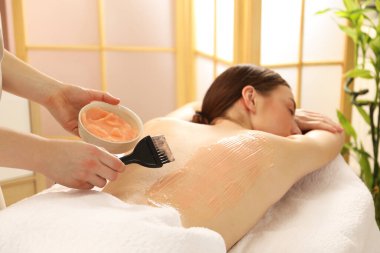 Vücut sargısı için kozmetik ürünler uygulayan estetikçi kaplıca salonundaki kadının sırtına sarıp kapatıyor.