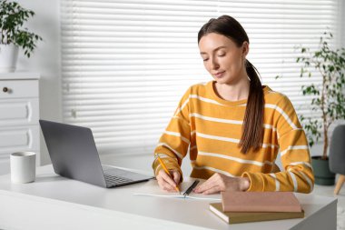 İçerideki masada ders sırasında not alan bir kadın. Kendi kendine çalışma.