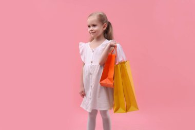 Pembe arka planda alışveriş torbaları olan küçük kız.