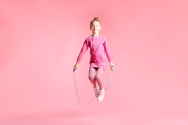 Cute little girl with jump rope on light pink background