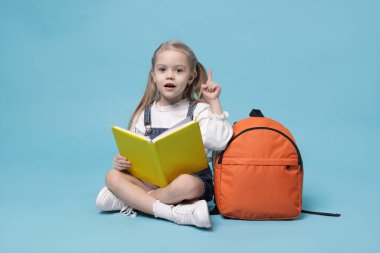Sırt çantası ve açık mavi arka plan kitabı olan tatlı bir kız öğrenci.