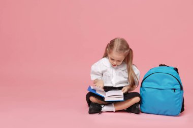 Sırt çantalı liseli kız pembe arka planda kitap okuyor. Metin için boşluk