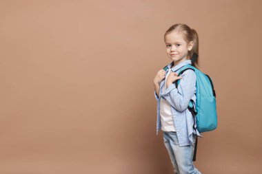 Kahverengi arka planda sırt çantası olan tatlı bir kız öğrenci. Metin için boşluk