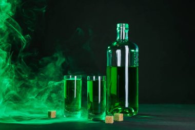 Absinthe shot bardakları, şişe ve esmer şeker siyah arka planda dumanlı