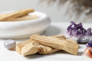 Palo Santo sopaları ve değerli taşlar beyaz masada, yakın plan.