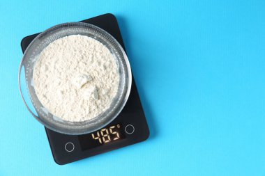 Açık mavi zemin üzerinde un bulunan elektronik mutfak terazisi, üst manzara. Metin için boşluk