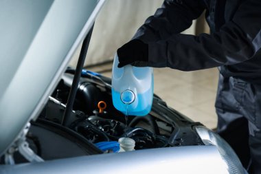 Plastik kutudan araba deposuna cam temizleyici döken bir adam var.