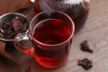 Cam fincanda leziz amber çayı, çaydanlık ve ahşap masada kuru gül sepalleri, yakın plan.