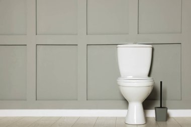 Ceramic toilet bowl and brush near grey wall indoors