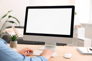 Kapalı alandaki ahşap masadaki boş ekranlı monitöre bakan bir kadın. Tasarım için model