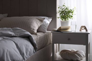 Yatağın yanında kitap, dekor ve bir bardak su olan komodin.