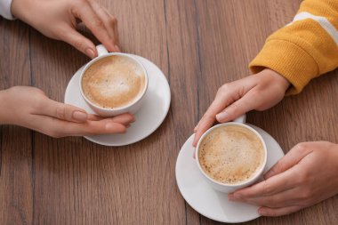 Kahve molası. Ahşap masada elinde sıcak içecekler olan kadınlar, yakın plan.