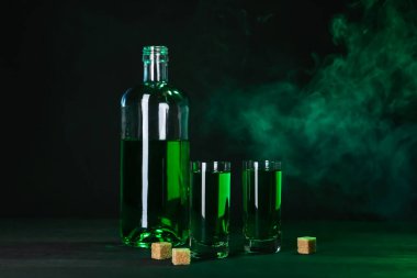 Absinthe shot bardakları, şişe ve esmer şeker siyah arka planda dumanlı