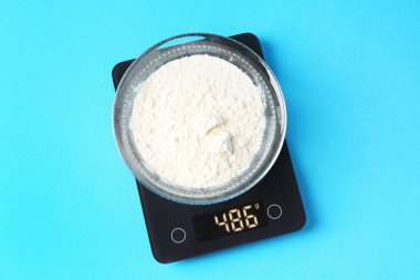 Açık mavi zemin üzerinde un bulunan elektronik mutfak terazisi, üst görünüm.