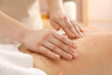 Vücut sargısı için kozmetik ürünler uygulayan estetikçi kaplıca salonundaki kadının sırtına sarıp kapatıyor.