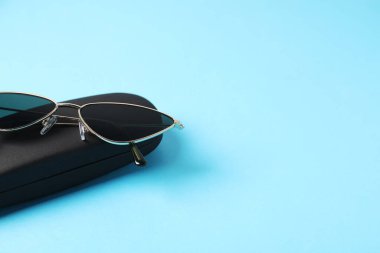 Açık mavi arka planda şık güneş gözlüklü çanta, yakın plan. Metin için boşluk