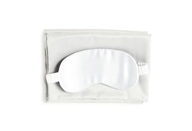 Beyaz arka planda ipek çarşaflar ve uyku maskesi, üst manzara.