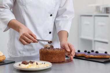 Pasta şefi mutfaktaki masada çikolata parçacıklarıyla pasta dekore ediyor.