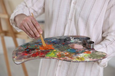 Sanatçının stüdyosunda boyaları palette karıştıran adam, yakın plan.