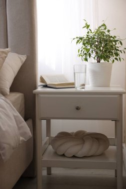 Yatağın yanında kitap, çiçek ve bir bardak su olan komodin.