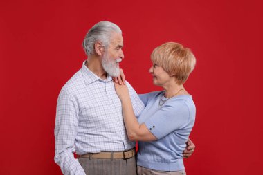 Kırmızı arka planda birbirlerine bakan sevimli yaşlı çift.