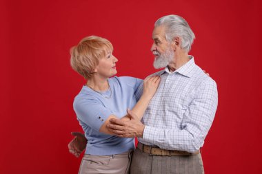 Kırmızı arka planda birbirlerine bakan sevimli yaşlı çift.