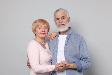 Gri arka planda el ele tutuşan sevimli yaşlı çiftin portresi.