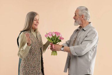 Adam bej arka planda mutlu karısına pembe lale buketi sunuyor.