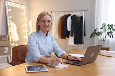 Dükkan sahibi terzisindeki masada dizüstü bilgisayarla çalışırken not alıyor.