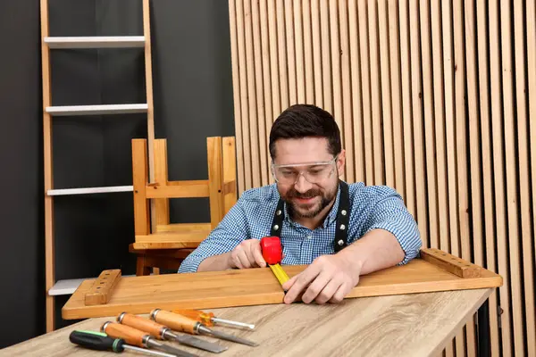 Rahatlatıcı hobi. Gülen adam atölyedeki bantla ahşap kalas ölçüyor.