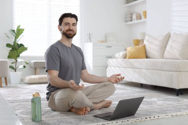 Gülümseyen adam evde laptopun önünde meditasyon yapıyor.