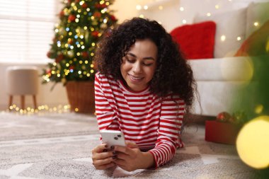 Evde akıllı telefon kullanan mutlu genç bir kadın. Noel kutlaması