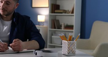 Kendi kendine çalışma. İçerideki masada ders sırasında not alan bir adam. Kamera sola hareket ediyor