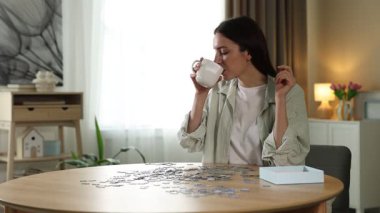 Ahşap masada yapboz çözerken çay içen kadın.